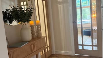 A hallway with a wooden bench, a mirror, a vase with a plant, a candle, and a door with glass panels.