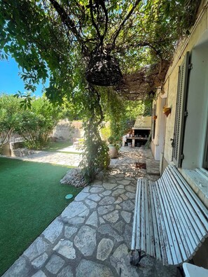 A stone-paved patio with a bench, a small outdoor kitchen, and a lush green lawn. - Cozy Mérindol Hideaway In the Heart of the Luberon (Mérindol)