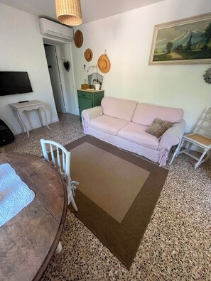 Ein Wohnzimmer mit einer Couch, einem Couchtisch, einem Fernseher und einem Gemälde an der Wand.