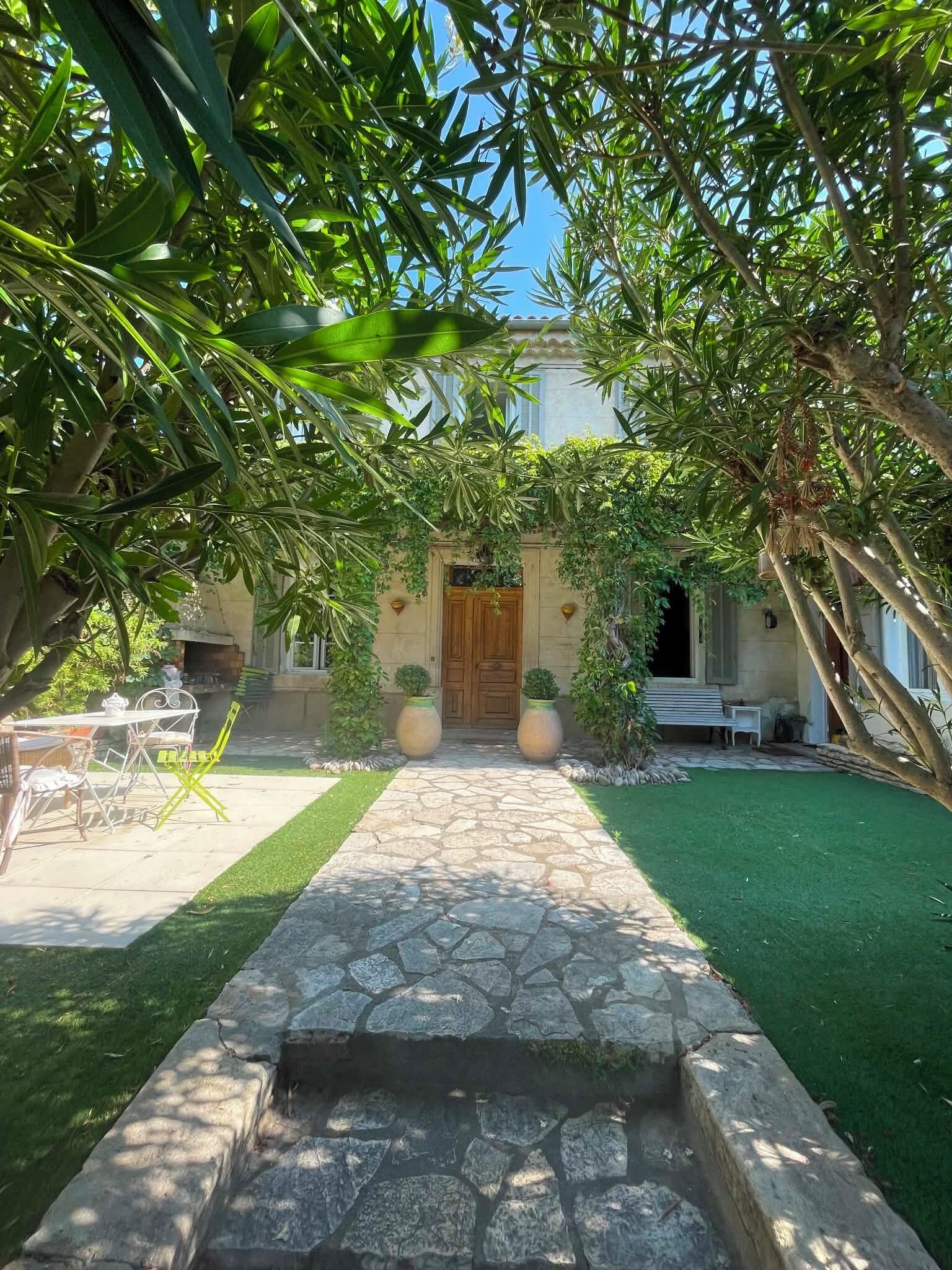 A stone pathway leading to a building with a wooden door, surrounded by greenery and a small lawn.