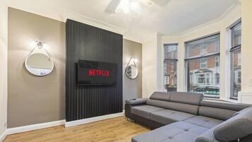 A modern living room with a grey sofa, a flat-screen TV mounted on a dark wall, and two wall-mounted mirrors.