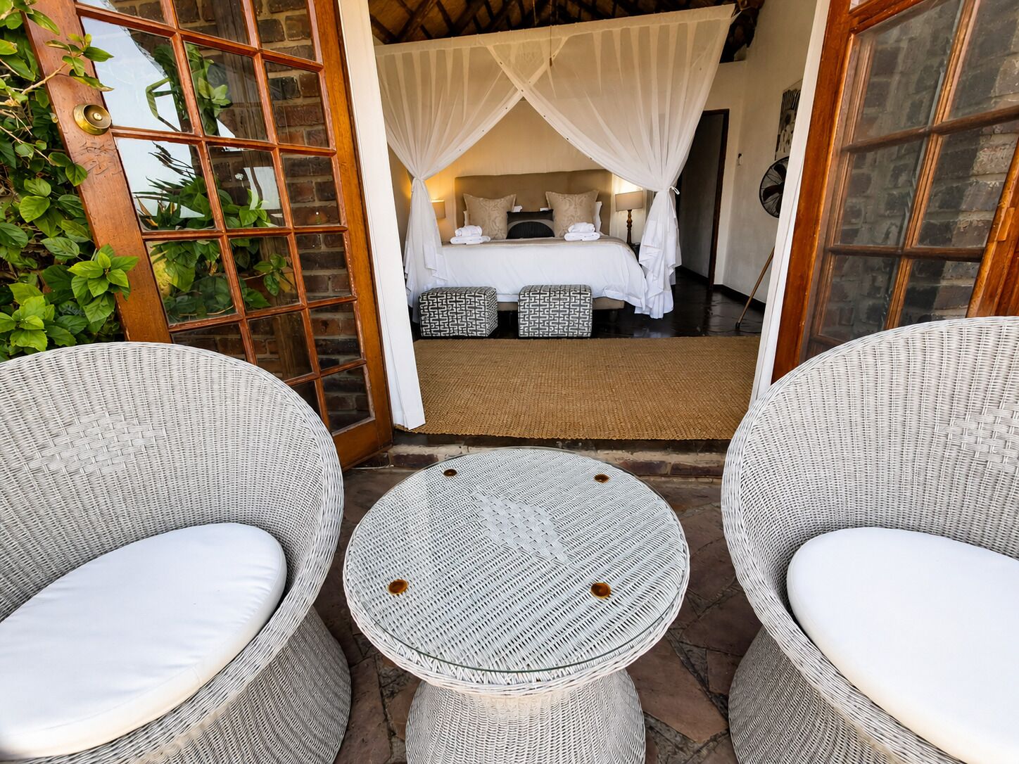 A room with a bed, a small table, and two wicker chairs.