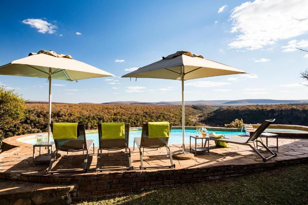 A poolside area with lounge chairs and umbrellas, overlooking a mountainous landscape.