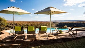 Zona de piscina con sillones de descanso y sombrillas, con vistas a un paisaje montañoso.