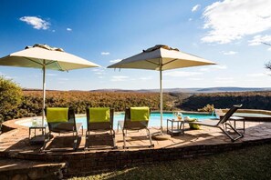 Un espace aménagé au bord de la piscine, avec des chaises longues et des parasols, offrant une vue sur un paysage montagneux.