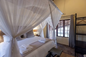 A bedroom with a four-poster bed, a bedside table with a lamp, and a window with curtains. - Magari Safari Lodge (Waterberg, Melkrivier)