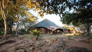 Un refugio rústico con techo de paja, rodeado por un paisaje natural con rocas y árboles.