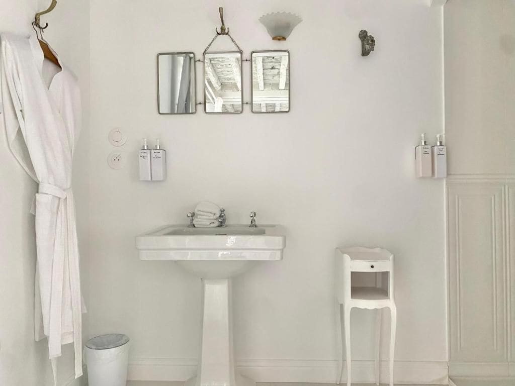 A bathroom with a pedestal sink, a towel rack, a small white stool, and a mirror with three rectangular mirrors above it.