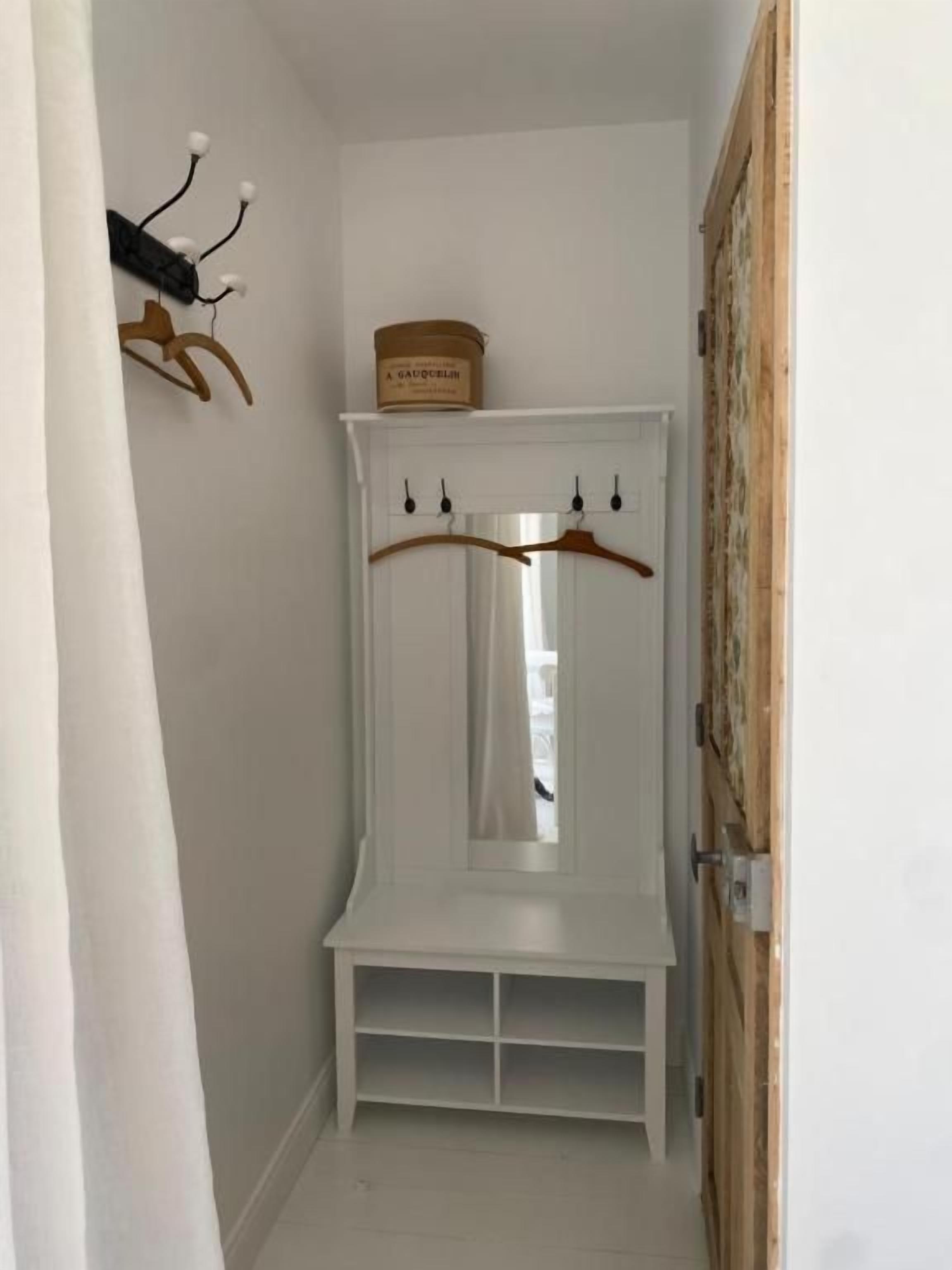 Un pasillo estrecho con un perchero blanco, una puerta de madera y un banco blanco.