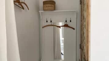 Un pasillo estrecho con un perchero blanco, una puerta de madera y un banco blanco.