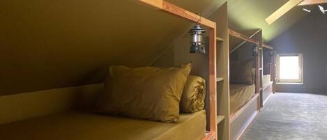 Un dormitorio tipo residencia con literas, un farol y una ventana que deja entrar luz natural.