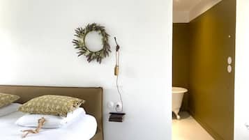 A bedroom with a bed, pillows, a wall-mounted light fixture, and a small shelf.