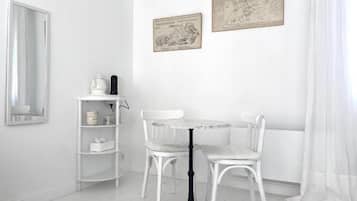 Un coin repas aux murs blancs, avec une table ronde et deux chaises, une étagère blanche où sont posés divers objets, et deux cartes encadrées accrochées au mur.