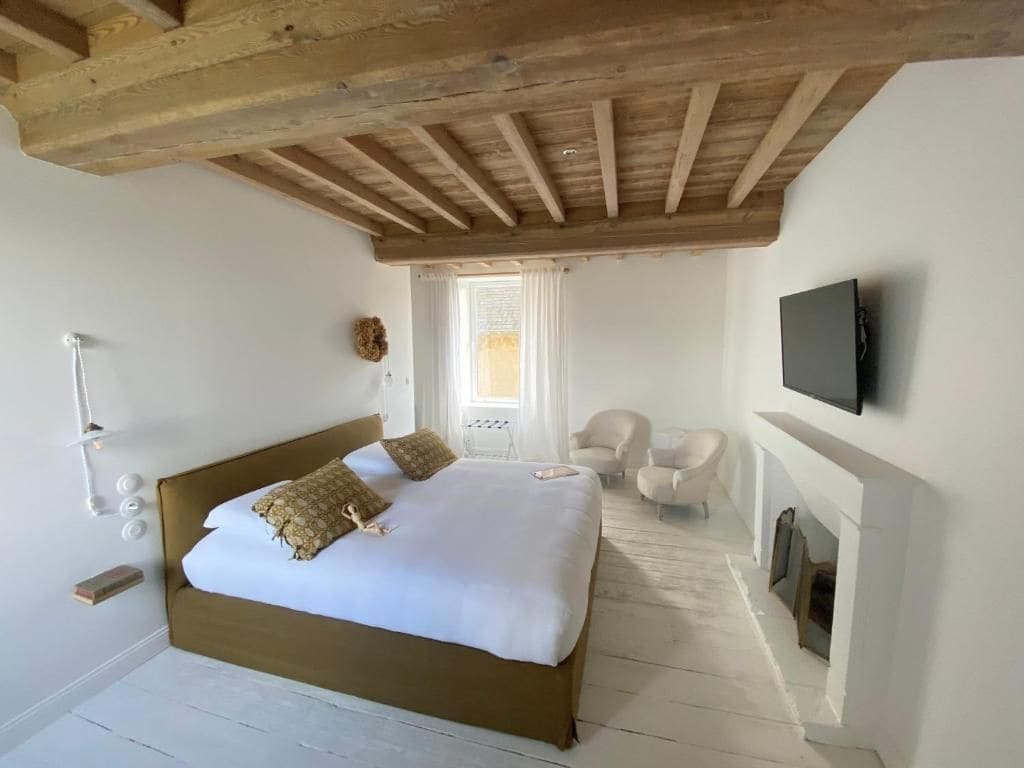 A bedroom with a large bed, a television mounted on the wall, and a fireplace.