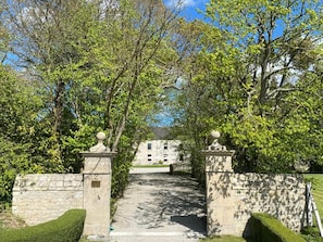 A stone gate leading to a building with a number '2' sign, surrounded by lush greenery.