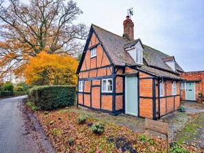 Ein traditionelles Fachwerkkotthaus mit erkennbarem Schornstein, einer Tür mit Hausnummer und einem Schild mit dem Namen 'Cricketers' Cottage'.
