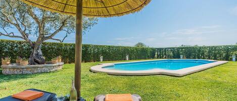 A backyard with a swimming pool, lounge chairs, and a large umbrella.