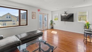 A spacious living room with a black leather sofa, a glass coffee table, and a flat-screen TV mounted on the wall. - 5 BR 5 Bath Home Bay side 10 people 2 Car parking (Seaside Heights)