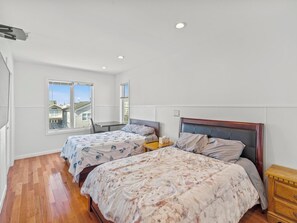 Une chambre avec deux lits, une commode en bois et une fenêtre donnant sur des maisons.