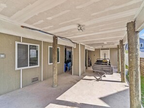 Un espace extérieur abrité, doté d’un sol en béton, de poteaux en bois et d’un gril en métal.