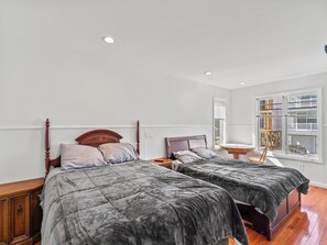 A bedroom with two beds, wooden headboards, a bedside table with a lamp, and a window with blinds. - 5 BR 5 Bath Home Bay side 10 people 2 Car parking (Seaside Heights)