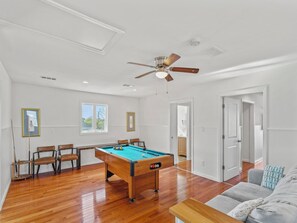 Une pièce spacieuse équipée d’une table de billard, d’un ventilateur de plafond et d’une porte donnant sur une autre pièce.
