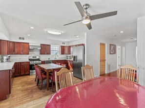 A modern kitchen with wooden cabinets, a stainless steel refrigerator, and a dining area with a red table and wooden chairs. - 5 BR 5 Bath Home Bay side 10 people 2 Car parking (Seaside Heights)