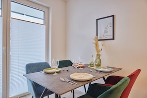 A dining area with a table set for four, chairs, and a window with blinds. - HomeME 1 & HomeME 2 Bad Oeynhausen (Bad Oeynhausen)