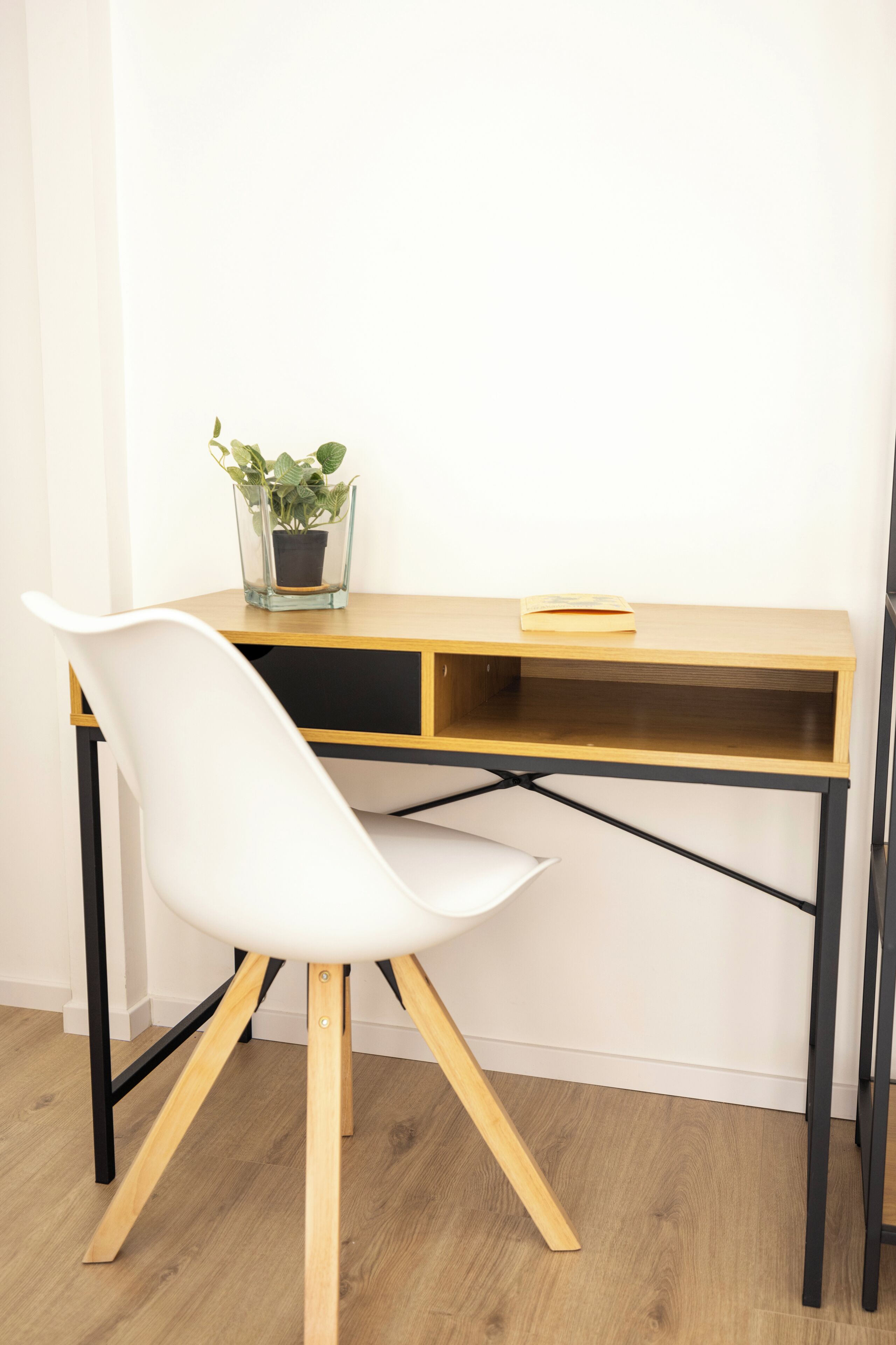 Un bureau moderne avec une chaise blanche, une petite plante en pot et un livre.