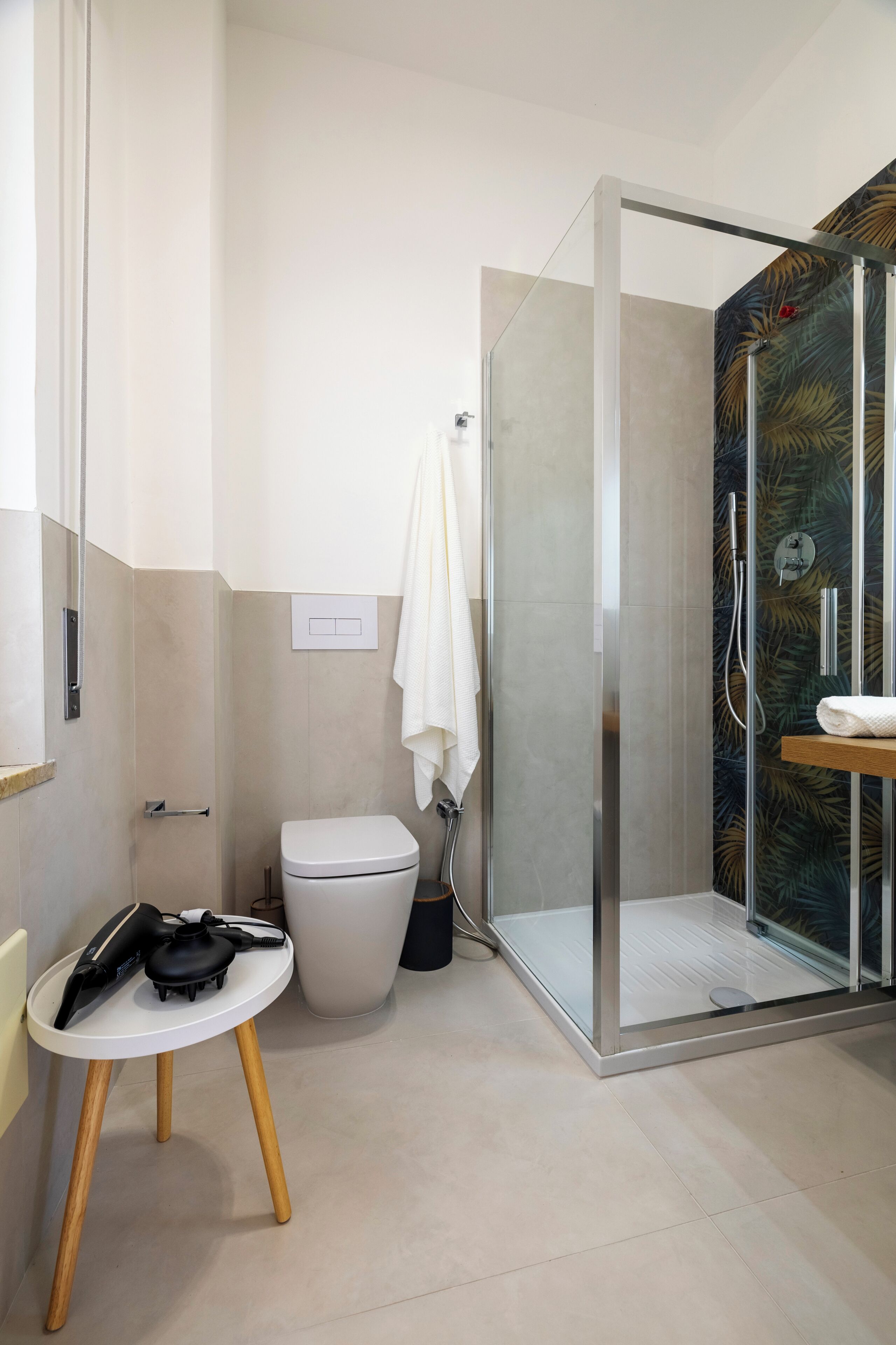 A modern bathroom with a glass-enclosed shower, a toilet, and a hairdryer on a small table.