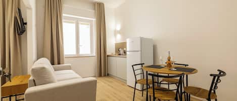 Un espacio habitable compacto con sofá, una mesa de comedor con sillas, una kitchenette y una ventana con cortinas.