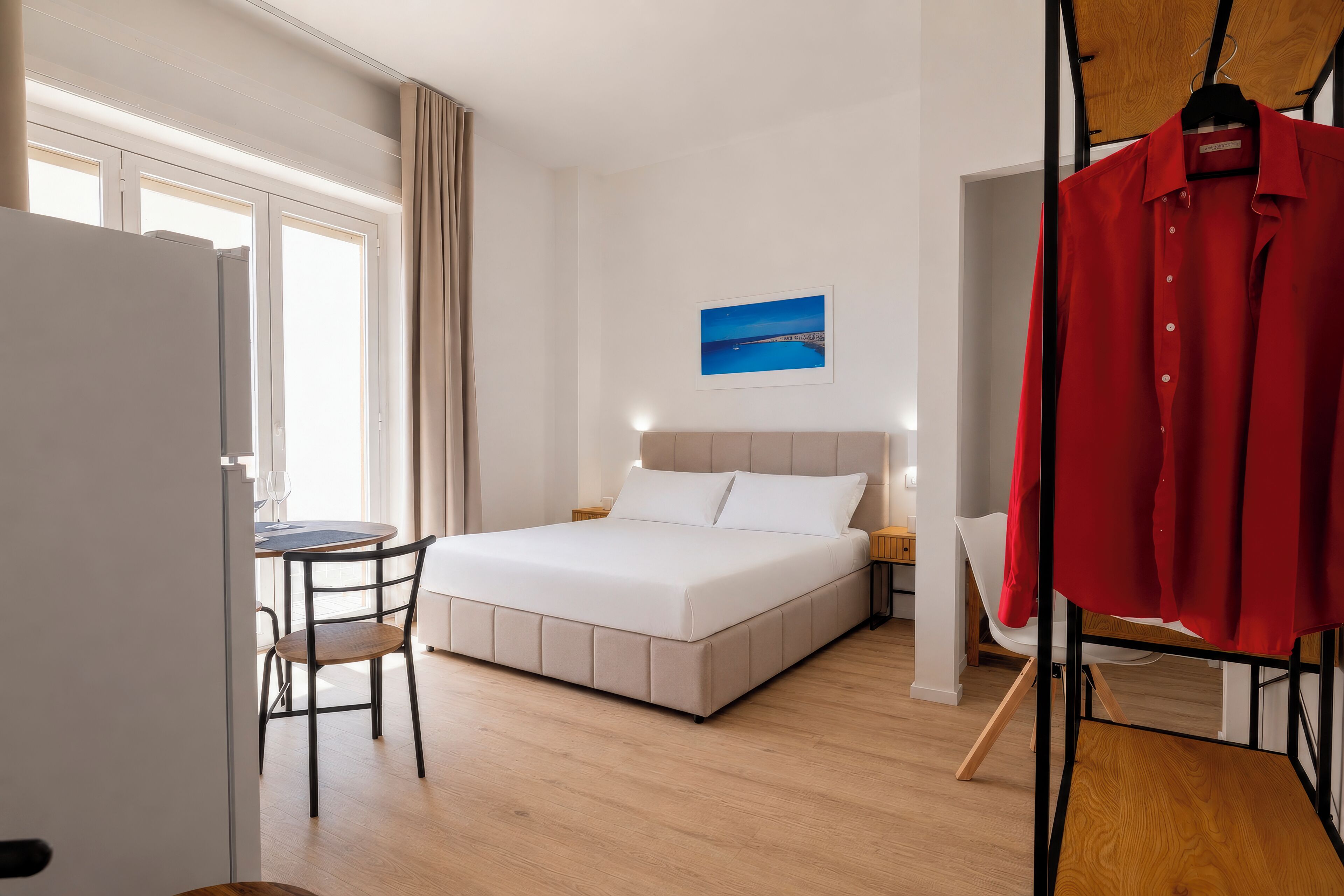 Een hotelkamer met een bed, een bureau, een stoel, een kledingkast en een schilderij aan de muur.