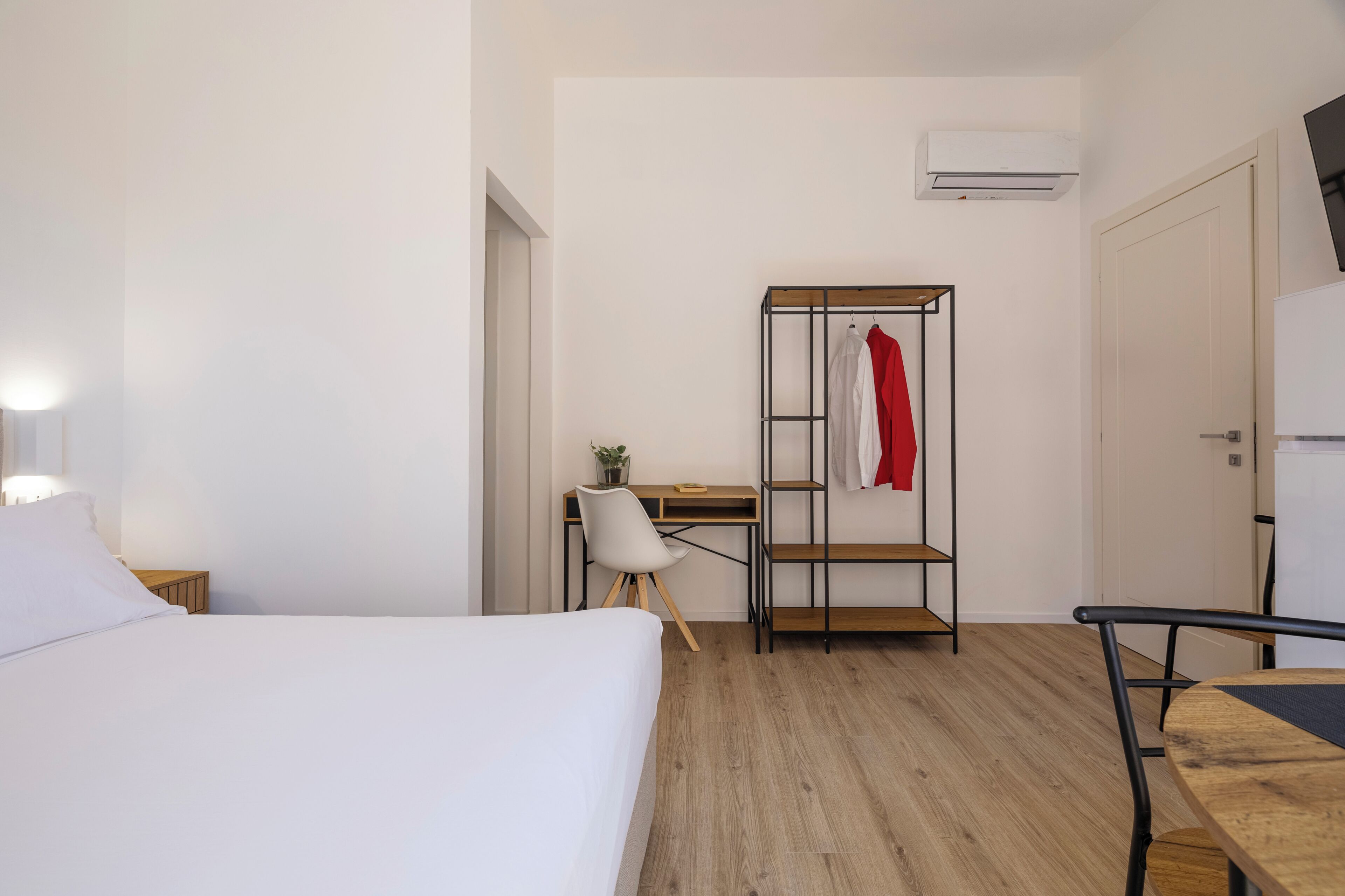 Een slaapkamer met een bed, een bureau, een stoel, een kledingkast en een airconditioning.