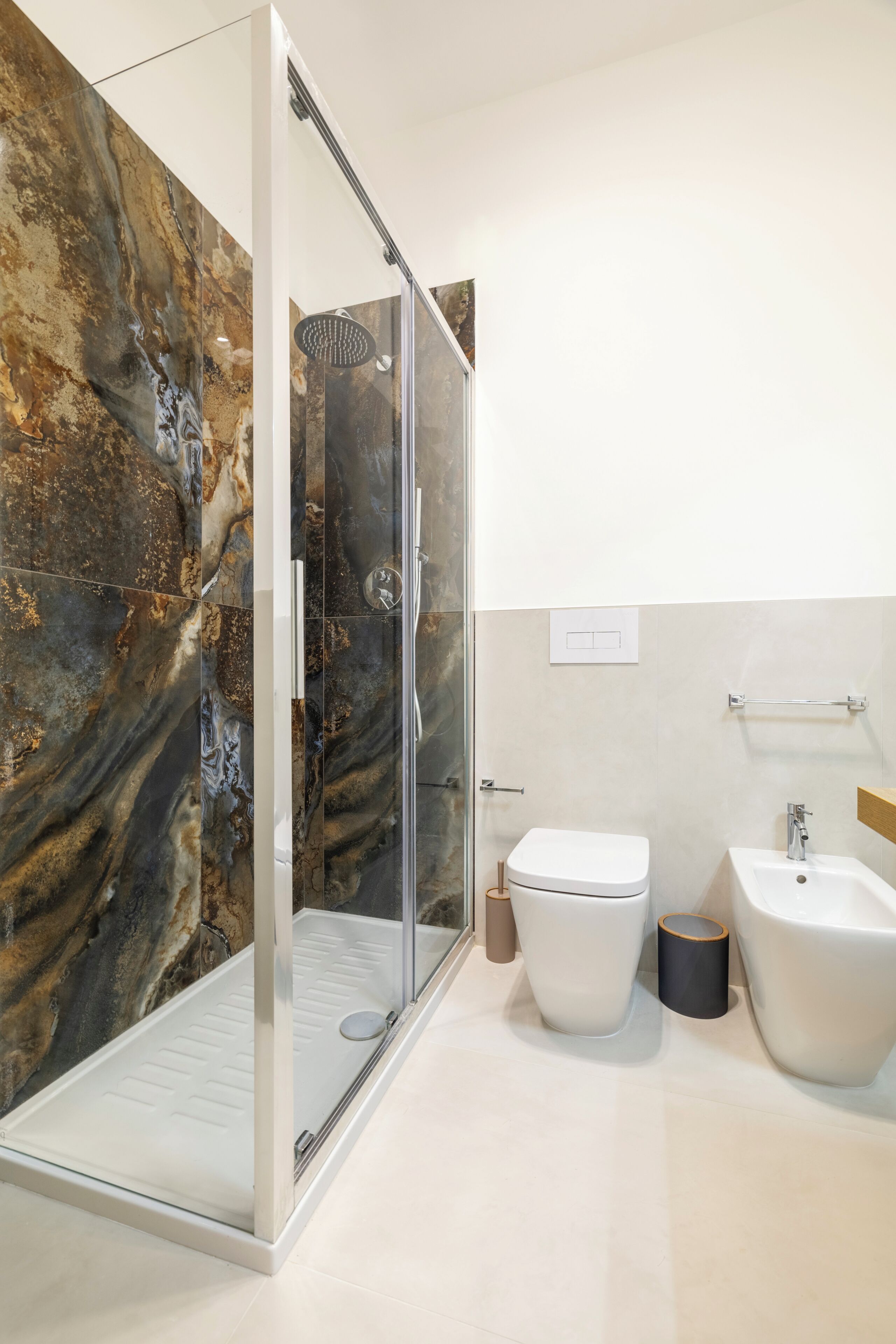 Een moderne badkamer met een douchecabine van glas, een toilet, een bidet en marmeren wanden.