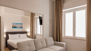 A hotel room with a bed, a sofa, a painting, a TV, and a window with curtains.