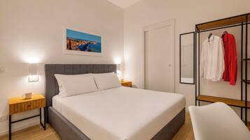 A hotel room with a bed, bedside tables, a nightstand, a bench, a wardrobe, a mirror, and a framed picture on the wall.