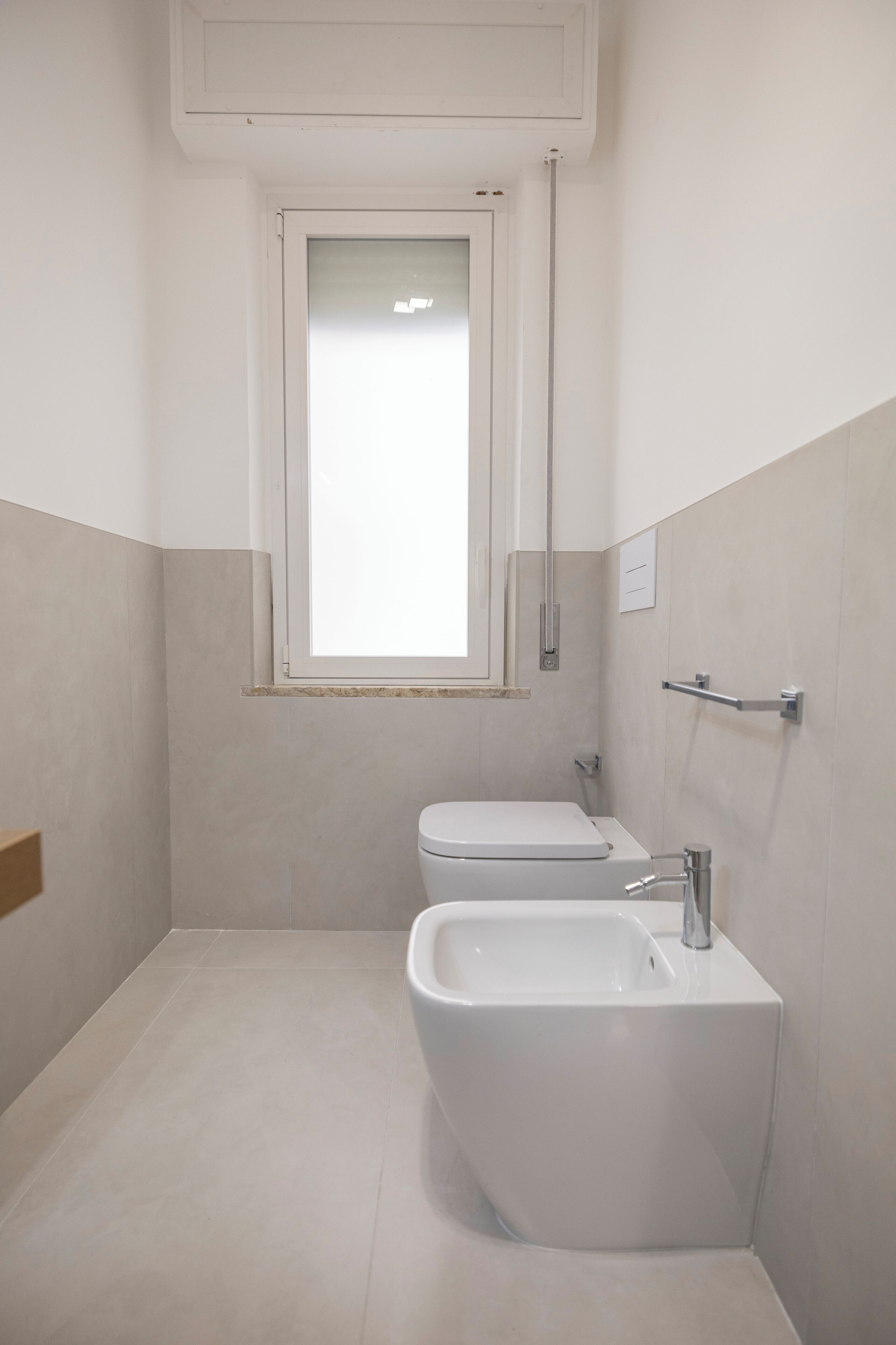 A small, modern bathroom with a toilet, bidet, and a window.