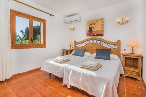 Ein Schlafzimmer mit einem Doppelbett, zwei Nachttischen, einem Fenster mit Vorhängen, einer Klimaanlage und einem Bild an der Wand.