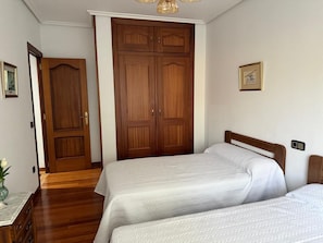 Un dormitorio con dos camas, un armario de madera y una puerta que da a otra habitación.