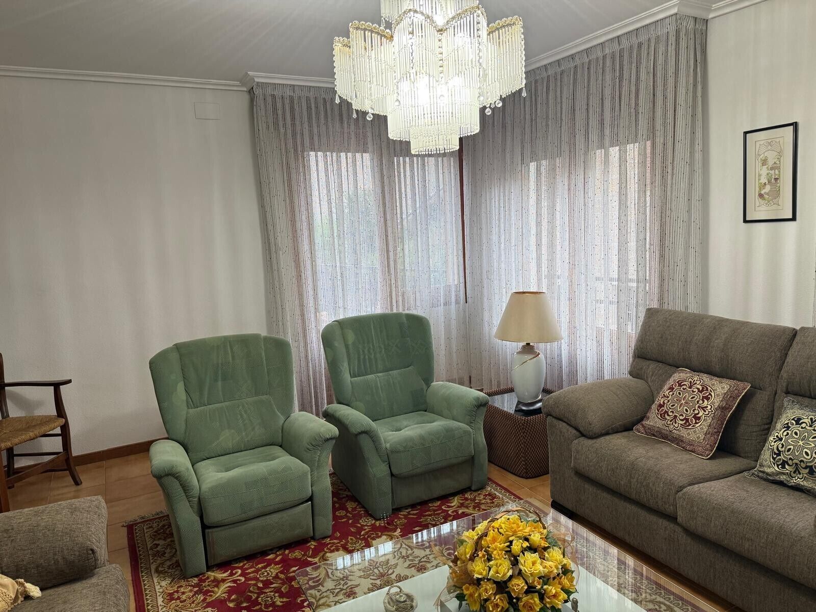A living room with a green armchair, a brown sofa, a lamp, and a vase of flowers.