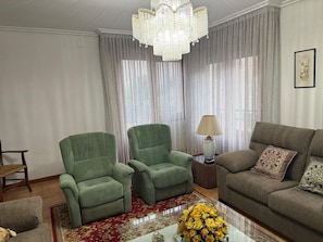 Una sala de estar con un sillón verde, un sofá marrón, una lámpara y un florero con flores.