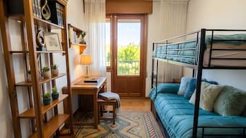 A room with a bunk bed, a wooden bookshelf, a desk with a lamp, and a patterned rug.