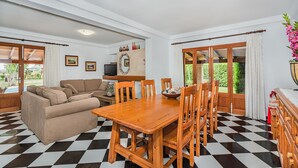 Un salon comprenant un canapé, une table à manger en bois avec des chaises, un téléviseur et une grande fenêtre avec des rideaux.