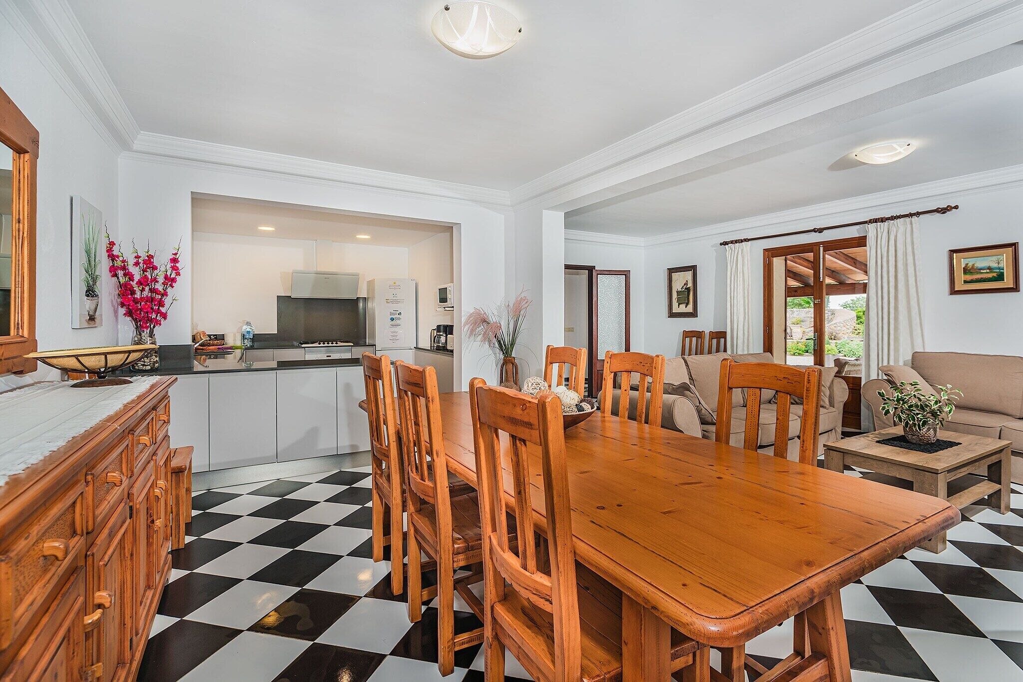 A dining area with a checkered floor, wooden chairs, a wooden table, and a kitchen in the background.