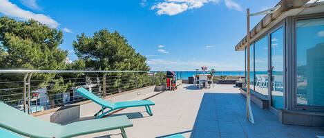 Eine Dachterrasse mit Liegestühlen, einem Tisch und Stühlen sowie Blick auf das Meer.