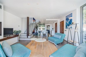 A modern living room with a flat-screen TV, seating area, and a staircase leading to an upper level. - Playa de Muro Chalet with Pool for 6 (Platja de Muro)