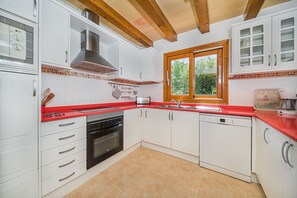 A kitchen with white cabinets, a red countertop, a Bosch dishwasher, and a window with a view of greenery. - Private Pool Villa in Pollensa (Pollensa / Pollença)