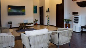 Un intérieur moderne avec des meubles en osier, un ordinateur portable posé sur une table en verre et des œuvres d’art accrochées aux murs.