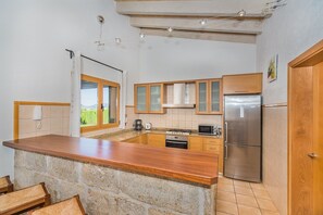 Eine kleine Küche mit Stein Arbeitsplatte, Holzschränken, einem Edelstahl-Kühlschrank und Blick durch ein Fenster.
