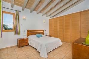 Un dormitorio con cama, mesitas de noche, armario, ventana con cortinas y vista al cielo.
